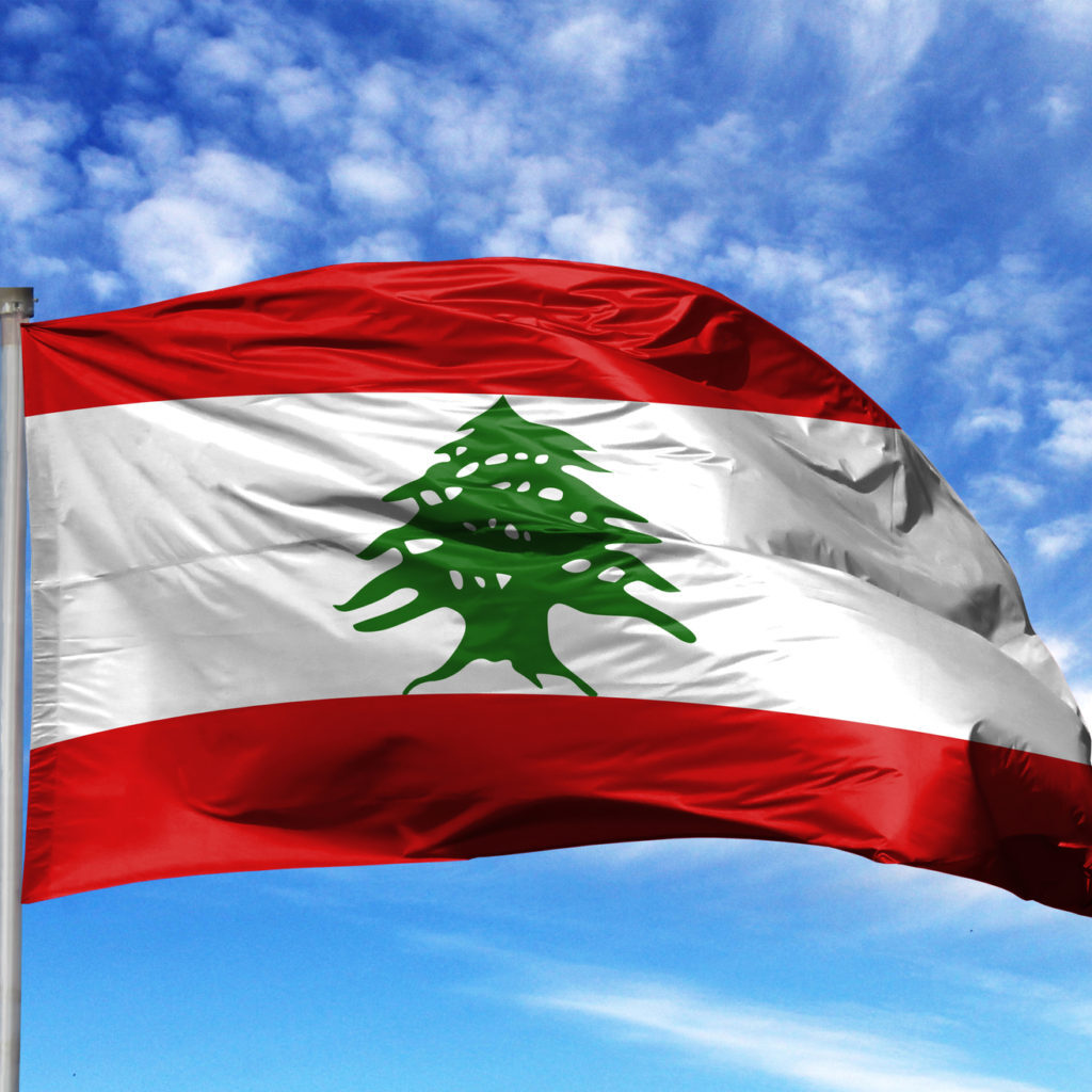 National flag of Lebanon on a flagpole in front of blue sky.